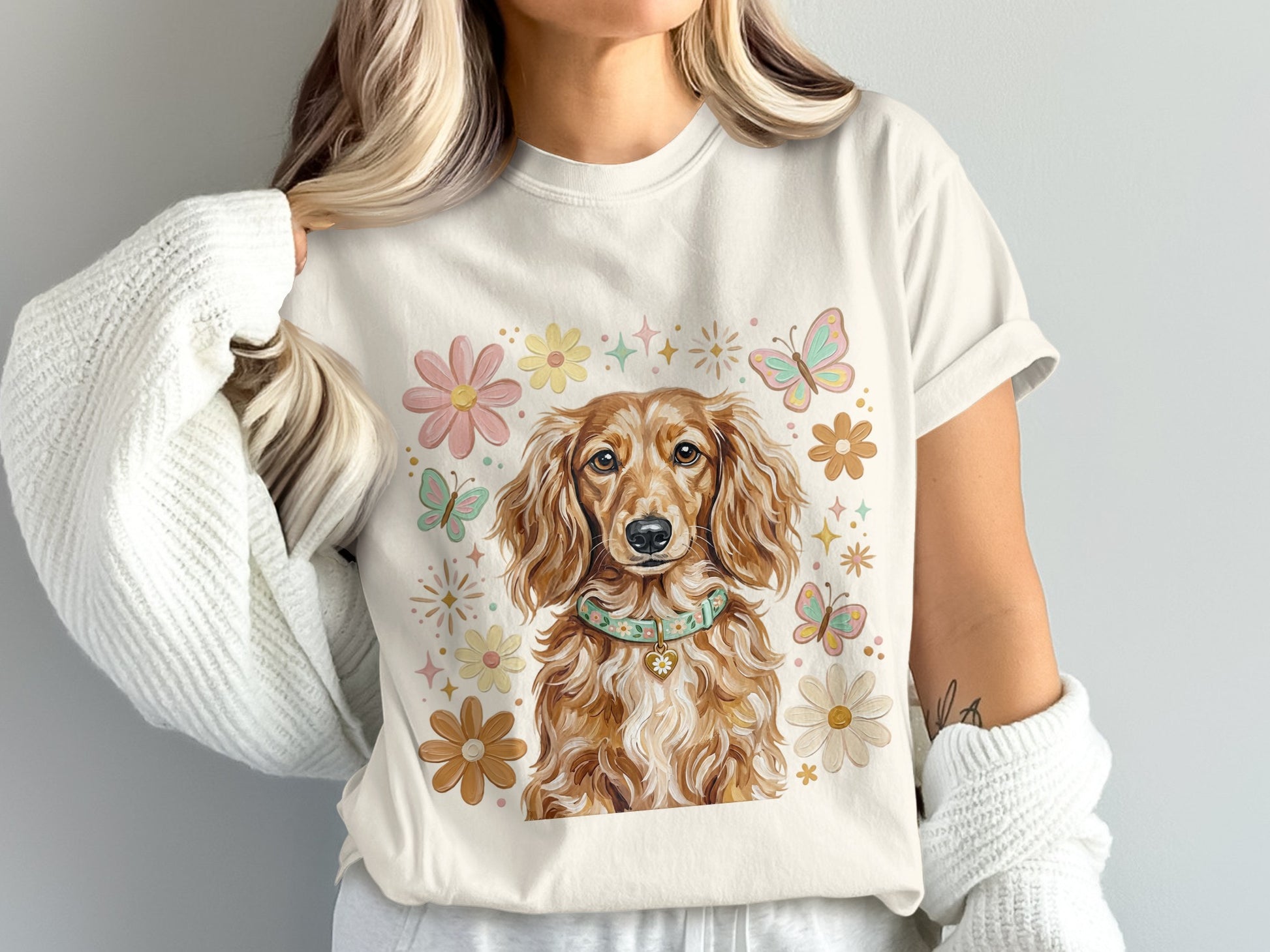 Cream t-shirt with a golden dachshund wearing a collar, surrounded by flowers and butterflies.