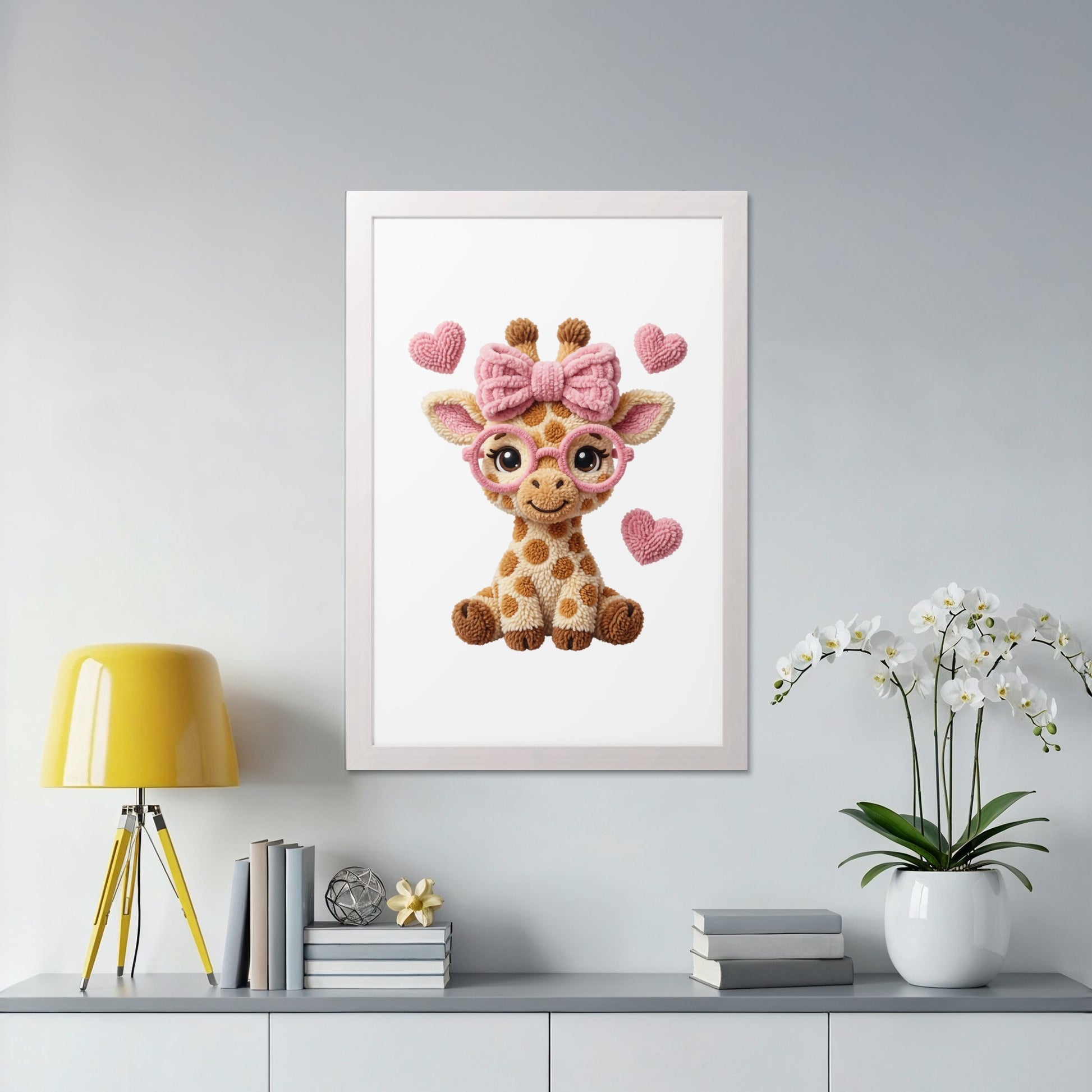 Crocheted baby giraffe with pink bows and heart glasses in a white frame.