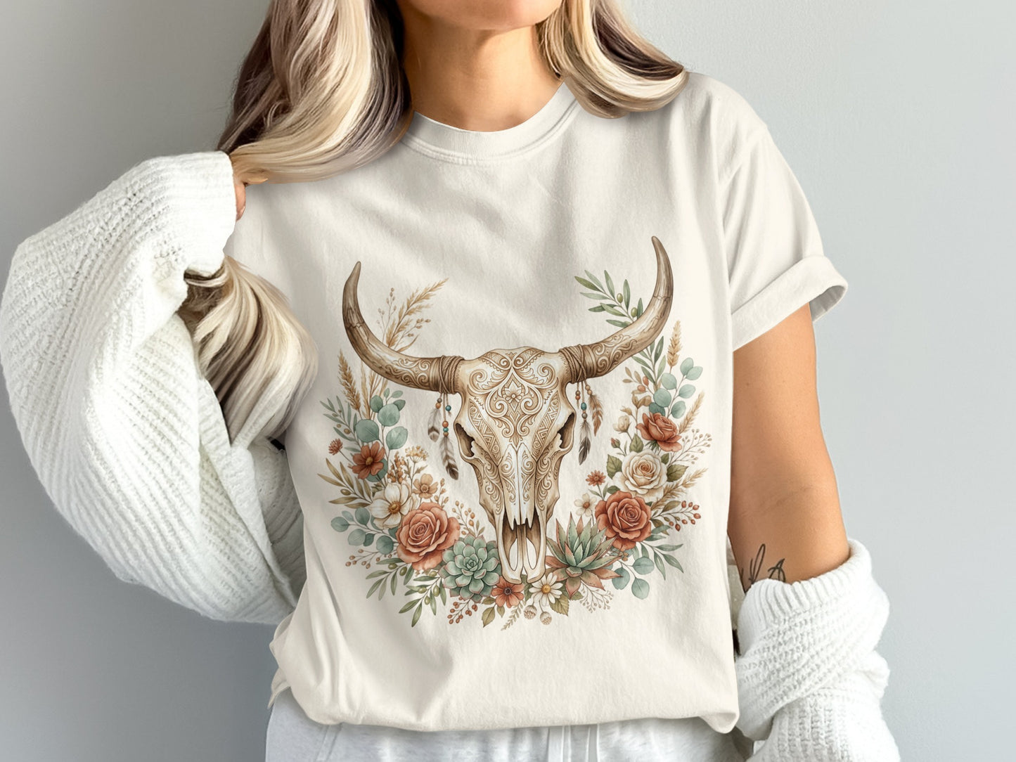 Cream t-shirt with a distressed skull adorned with flowers and feathers.