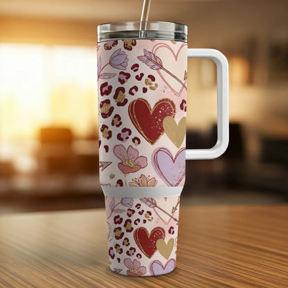 Pink leopard print tumbler with hearts and arrows, on a wooden table.