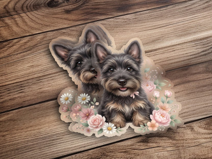 Two scruffy terrier puppies with pink bows surrounded by flowers.