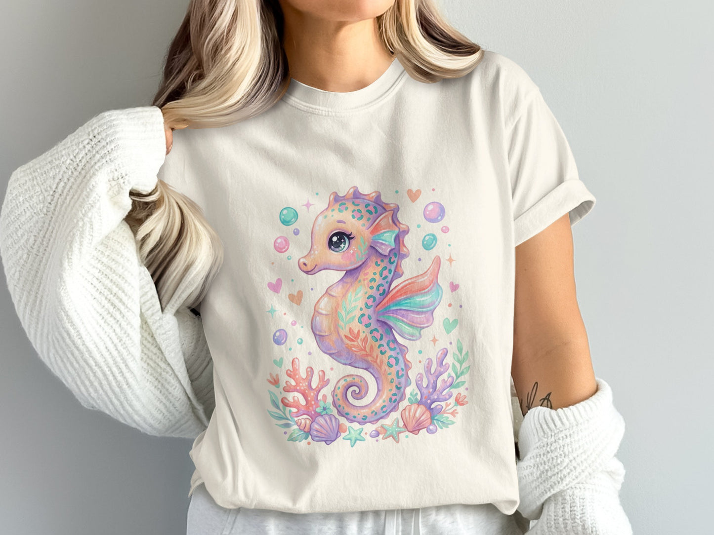 Cream t-shirt with a pastel watercolor seahorse, coral, and shells graphic.