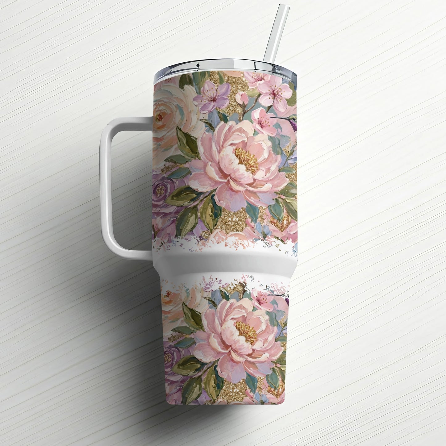 Floral patterned tumbler with handle and straw on a white wooden surface.