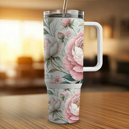 Tall floral tumbler with pink peonies and green leaves on a wooden surface.
