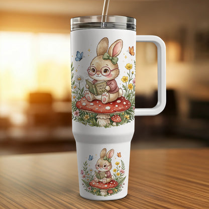 White tumbler with a bunny reading a book on a mushroom.