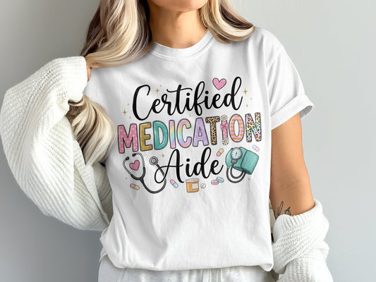 White t-shirt with "Certified Medication Aide" text, stethoscope, and medical symbols.