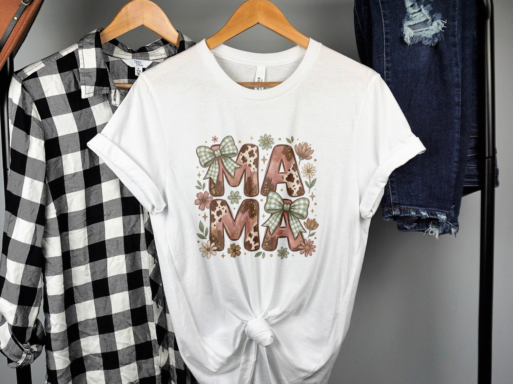 White t-shirt with "MAMA" in pink cow print and green bows.