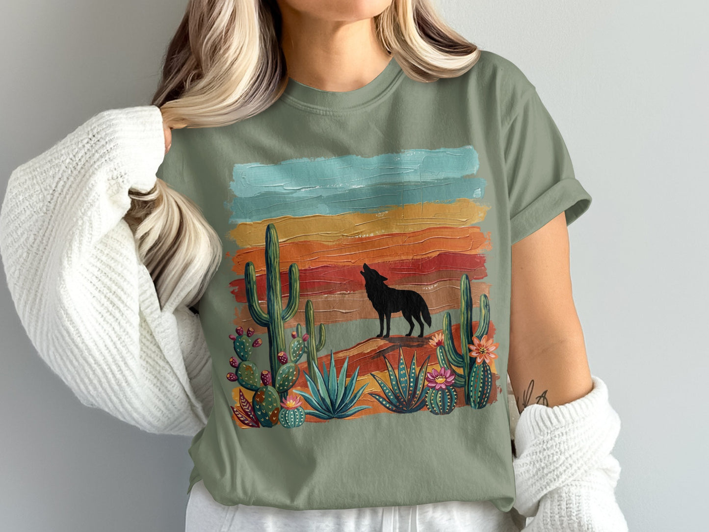 Green t-shirt with desert landscape featuring a wolf, cacti, and sunset stripes.