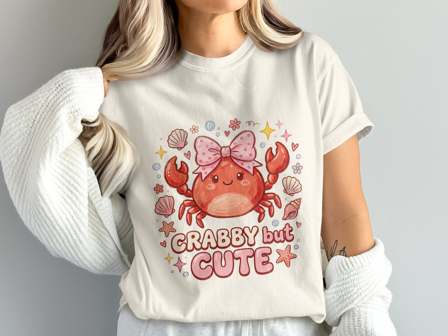 T-shirt featuring a smiling crab with a pink bow, text "CRABBY but CUTE".