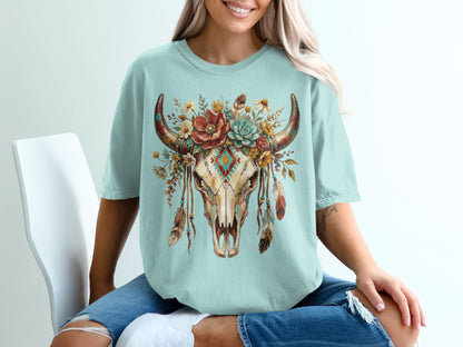 Cow skull with floral headdress and feathers on a light blue t-shirt.