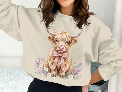 Cream sweatshirt with a Highland cow illustration wearing a pink bow and surrounded by flowers.