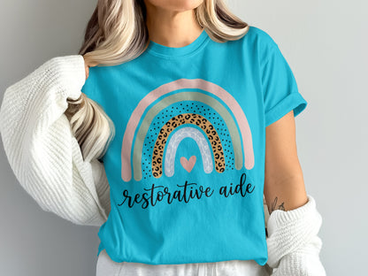 Turquoise t-shirt with a rainbow graphic and "restorative aide" text.