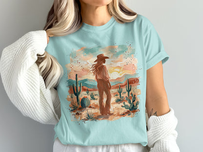 Light blue t-shirt with desert landscape graphic and woman in hat.