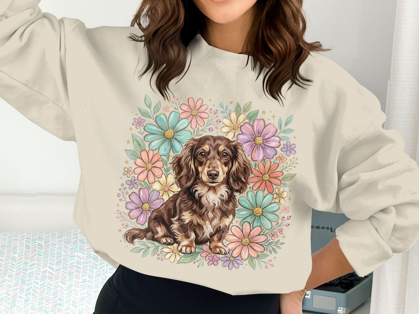 Dachshund dog surrounded by a colorful floral wreath on a cream sweatshirt.
