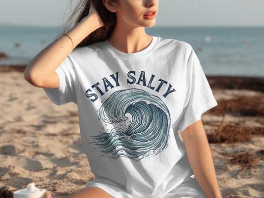 Woman wearing white t-shirt with "STAY SALTY" and wave graphic.