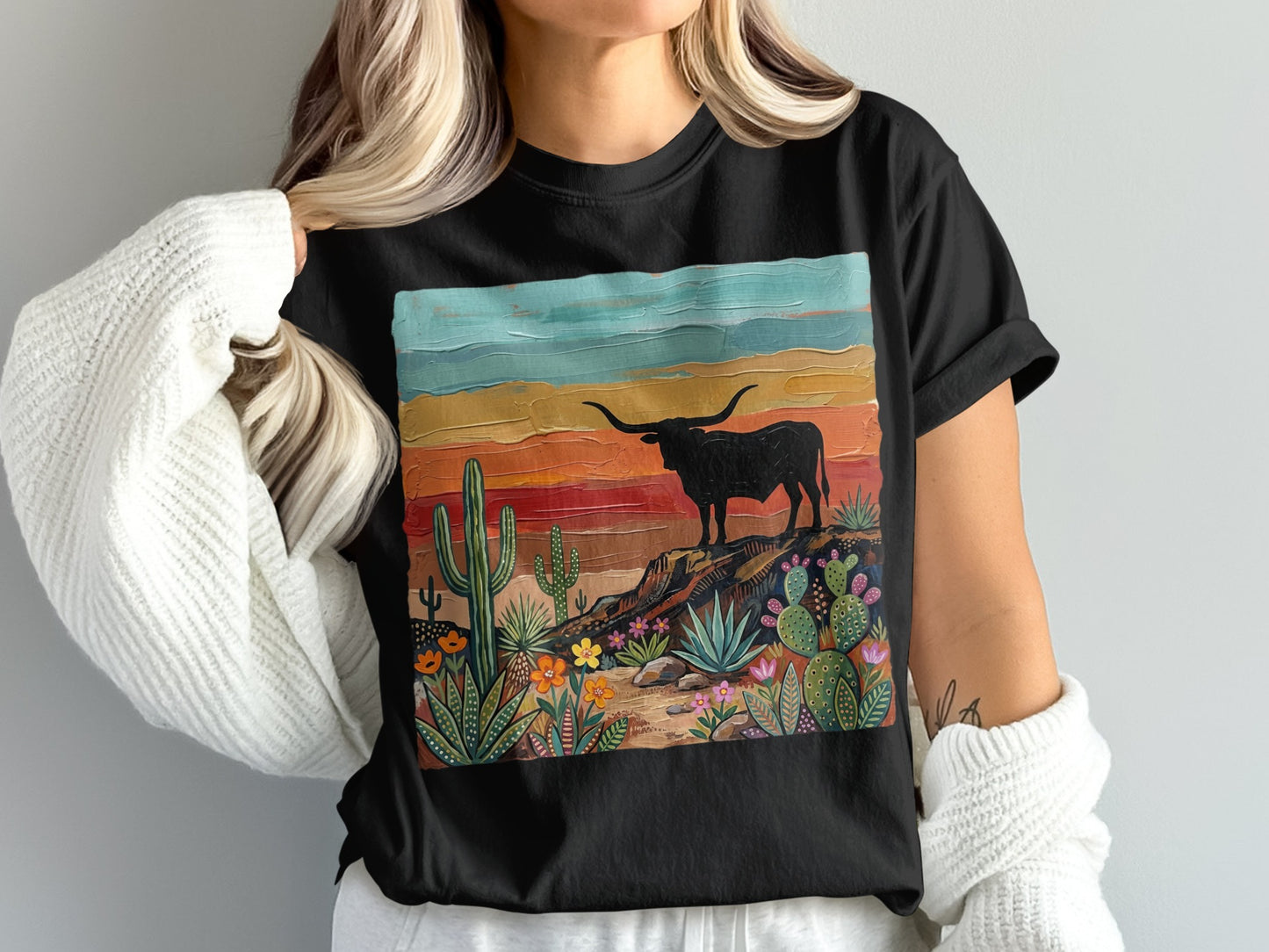 Black t-shirt featuring a longhorn bull on a rocky desert landscape with cacti and colorful sunset sky.