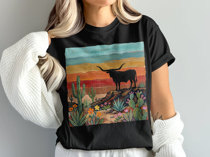 Black t-shirt featuring a longhorn bull on a rocky desert landscape with cacti and colorful sunset sky.