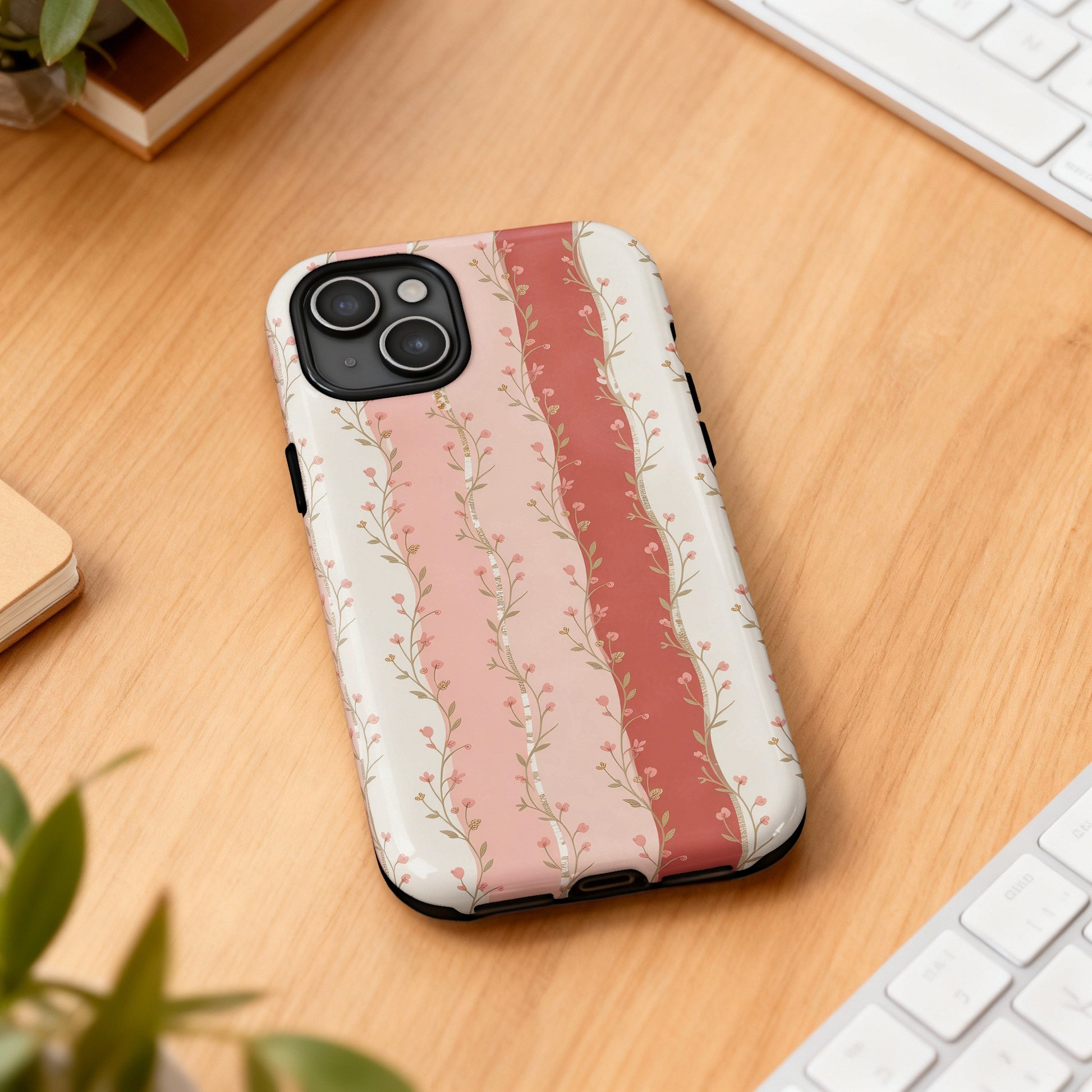 Floral phone case with pink and cream stripes on wooden surface.