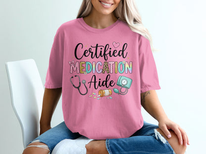 Pink t-shirt with "Certified Medication Aide" text and medical icons.