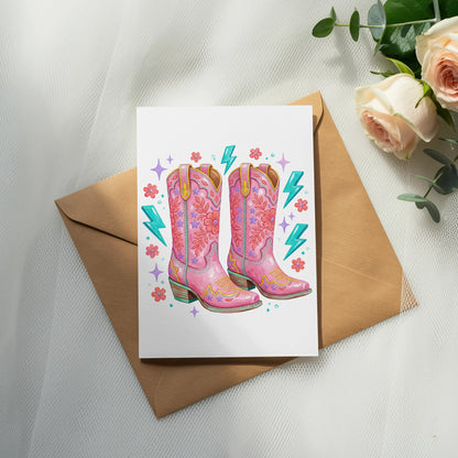 Pink cowboy boots with star and lightning bolt details on a card.