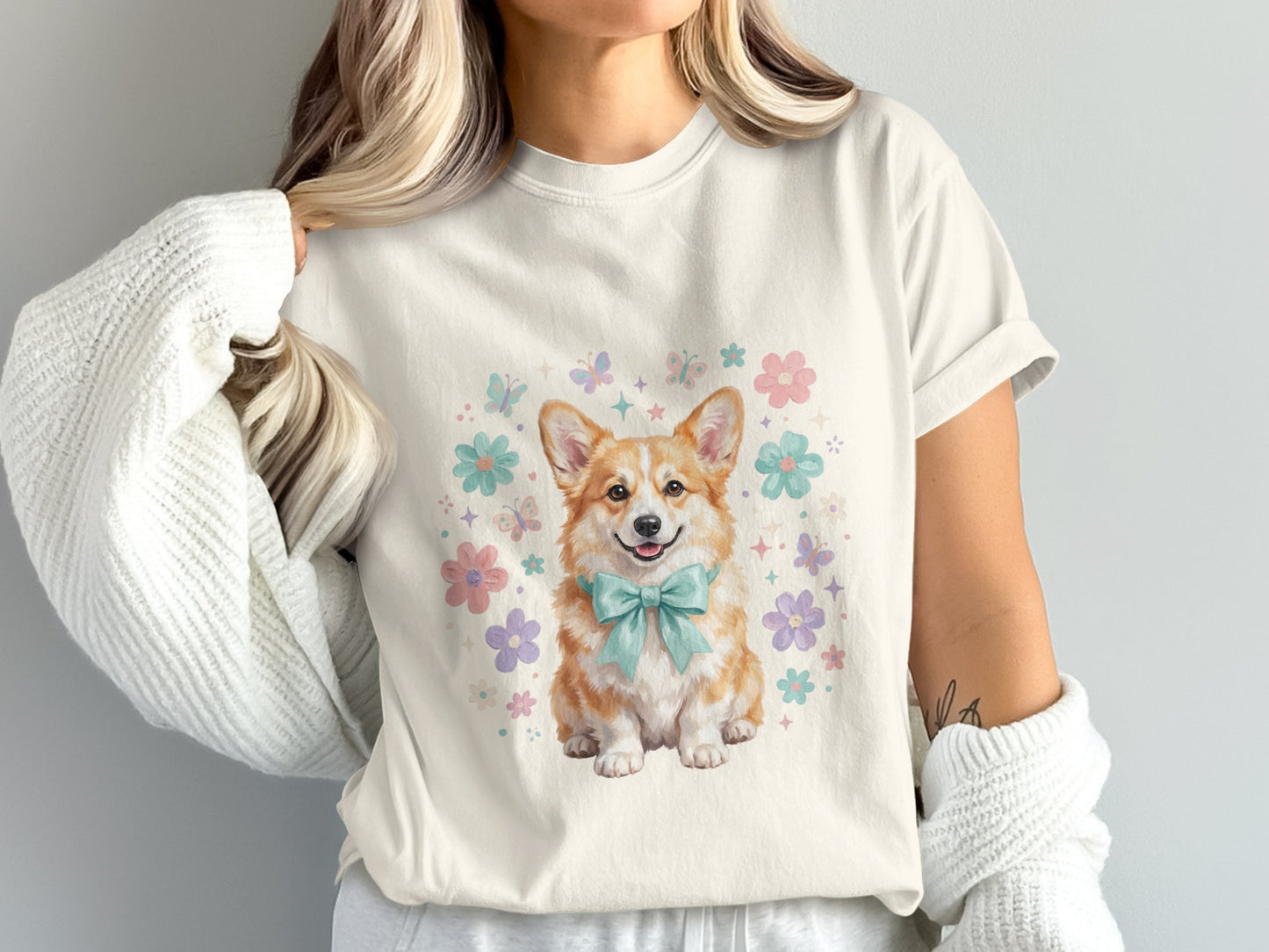 Cream t-shirt with a happy corgi wearing a blue bow tie and surrounded by flowers.