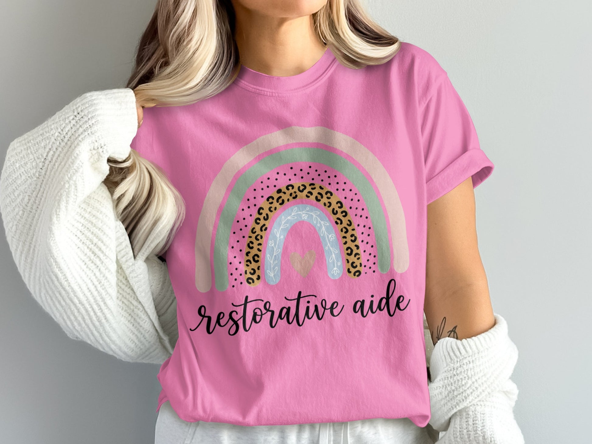 Pink t-shirt with a pastel rainbow and "restorative aide" text.