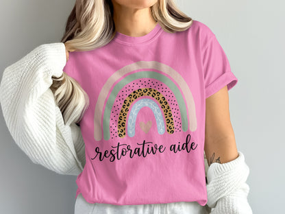 Pink t-shirt with a pastel rainbow and "restorative aide" text.