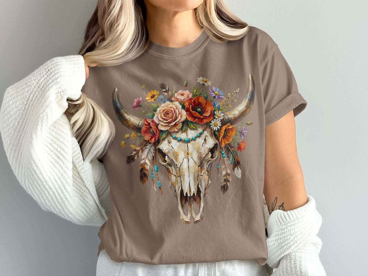 Brown t-shirt featuring a cow skull adorned with colorful flowers and feathers.