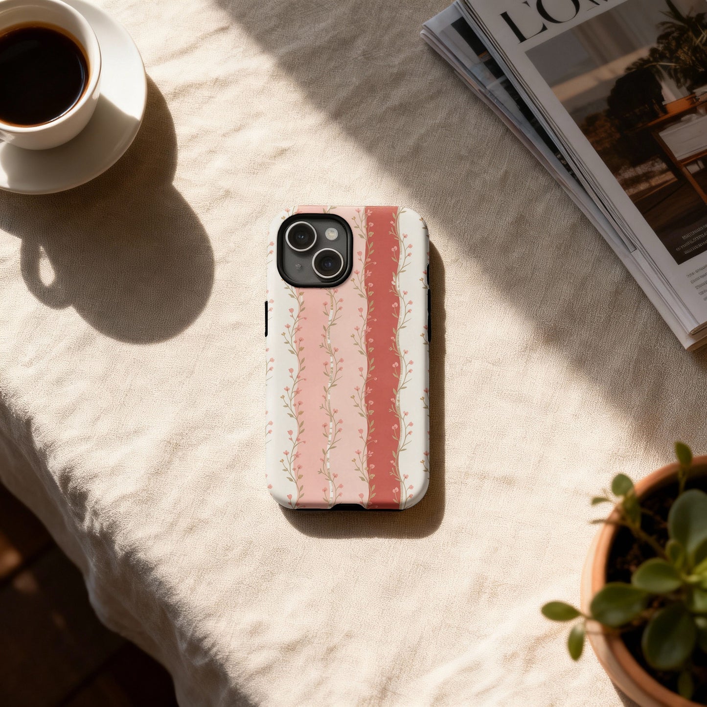 iPhone case with pink floral stripe pattern on a table with coffee and plant.