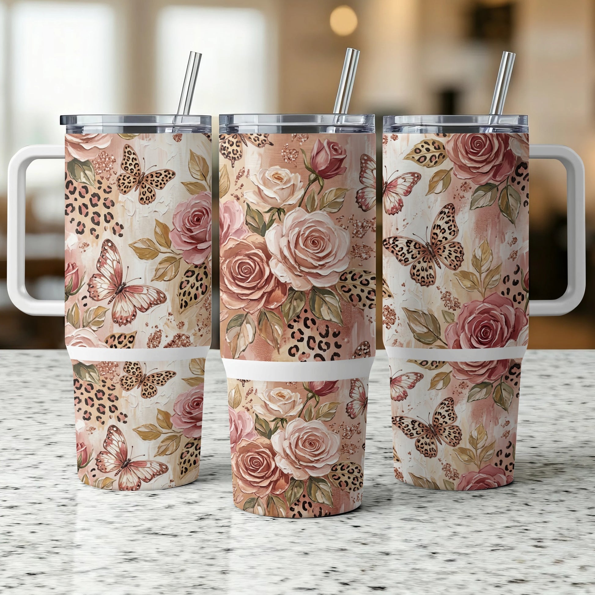 Three floral and butterfly tumblers with handles and straws on a counter.