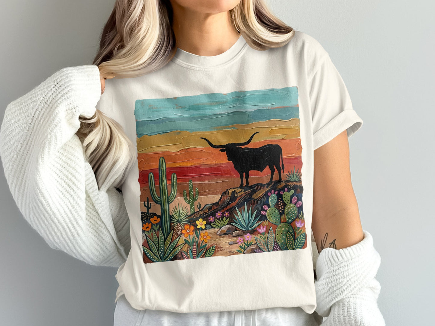 Woman wearing a t-shirt with a painted scene of a bull on a rocky desert landscape.