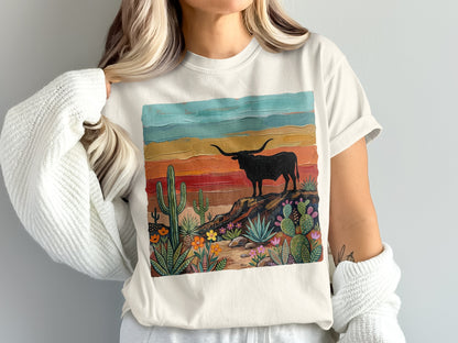 Woman wearing a t-shirt with a painted scene of a bull on a rocky desert landscape.