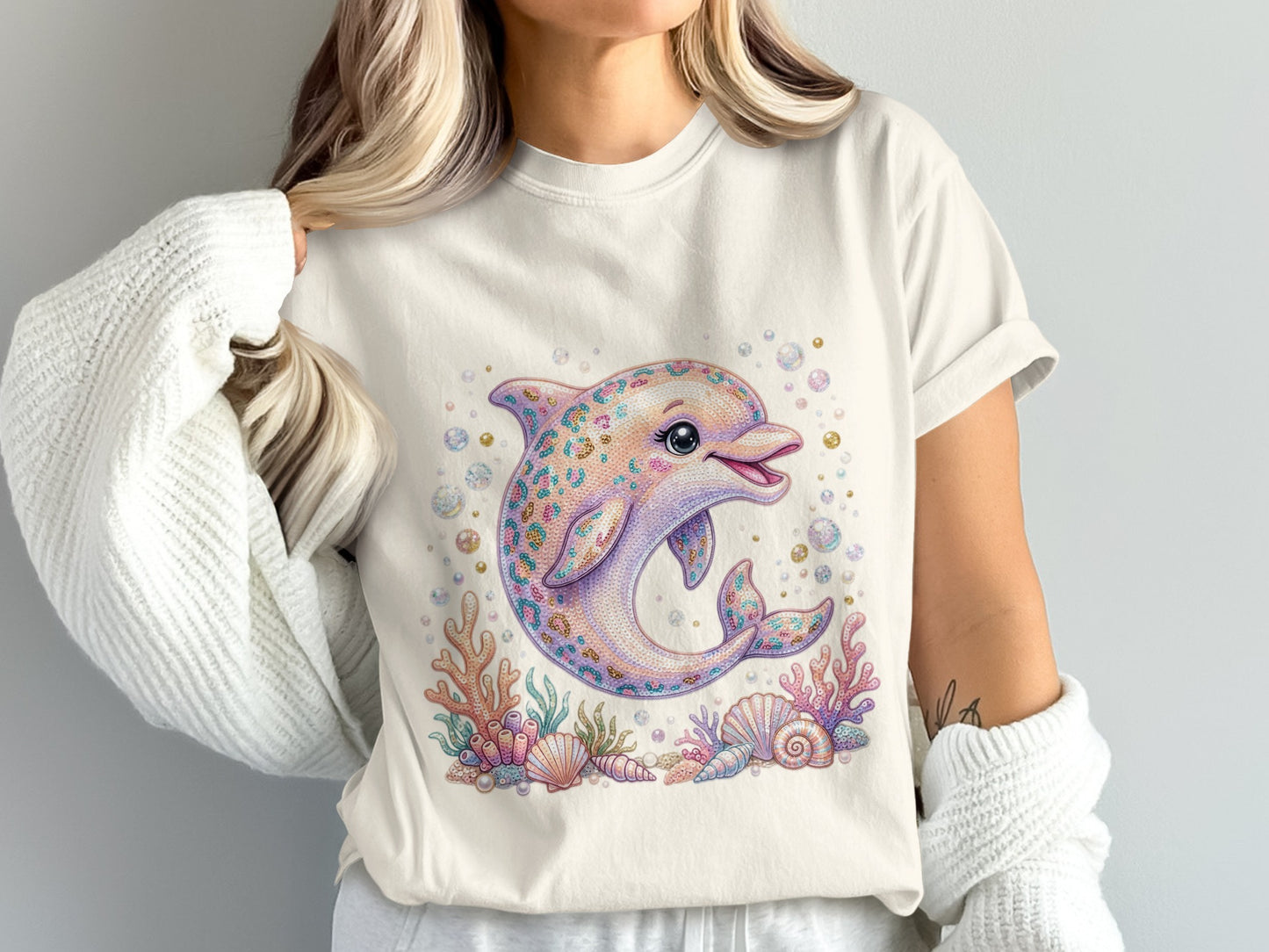 Cream t-shirt with a colorful, jeweled dolphin illustration surrounded by shells and coral.