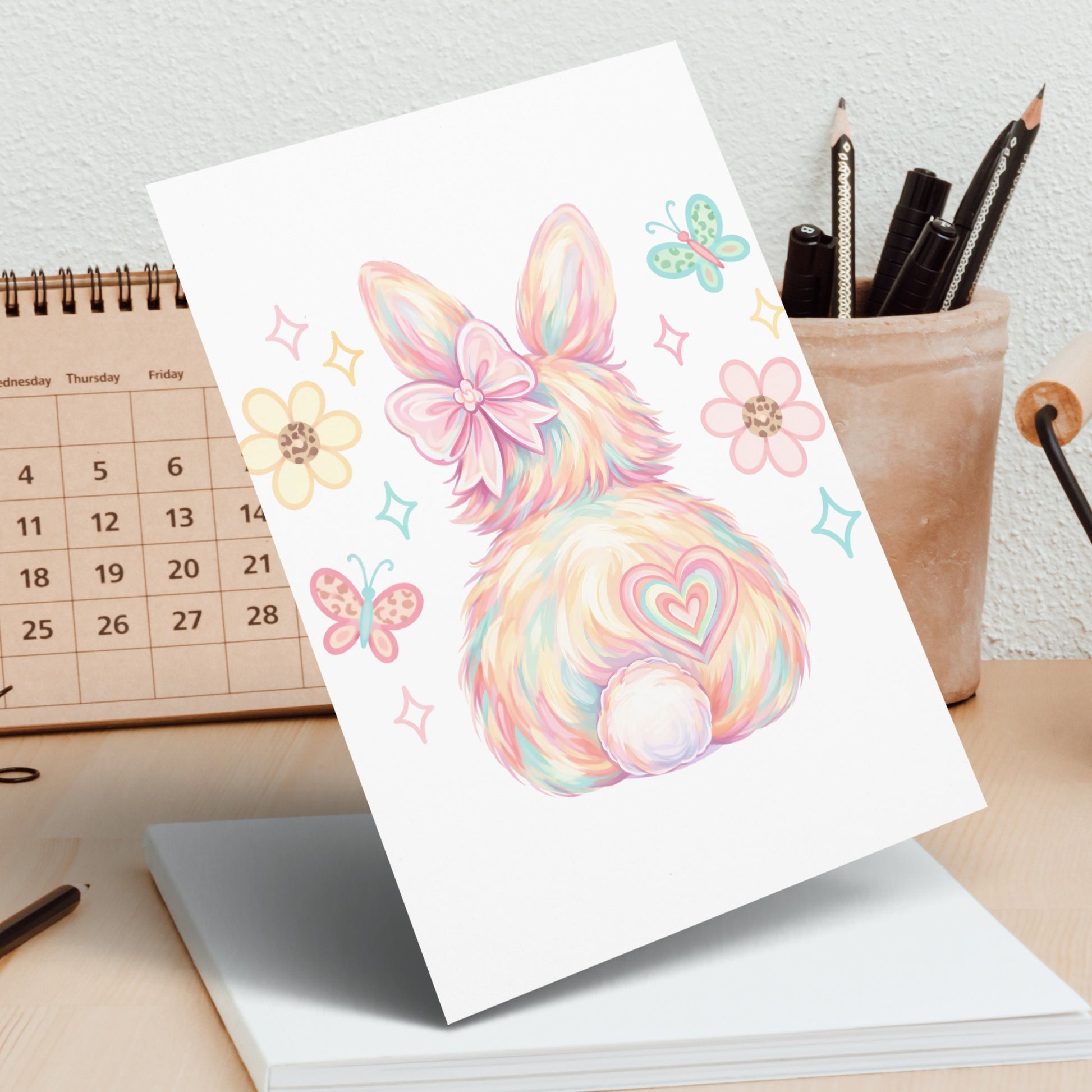 Fluffy bunny illustration with pastel colors and butterflies on a desk.