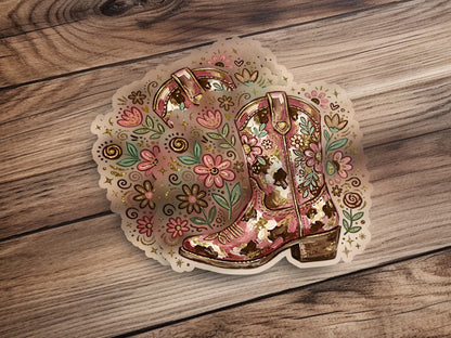 Pink and gold floral cowboy boot sticker on a wooden background.