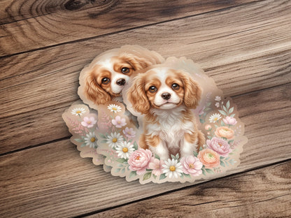 Two Cavalier King Charles Spaniels surrounded by soft pink and white flowers.