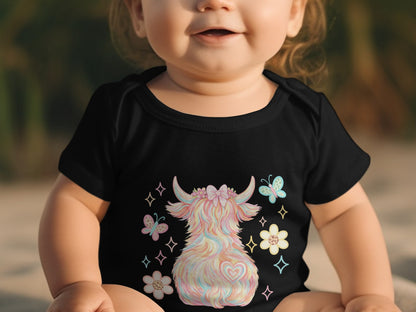 Baby wearing black onesie with fluffy pastel Highland cow and butterfly graphic.