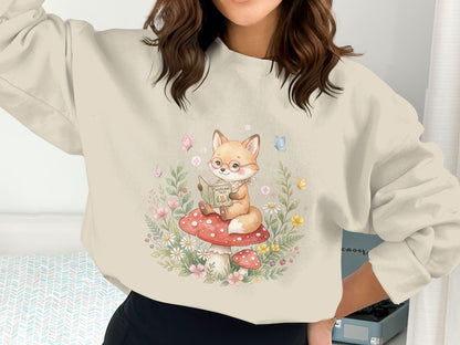 Sweatshirt with a fox reading a book on a mushroom, surrounded by flowers.