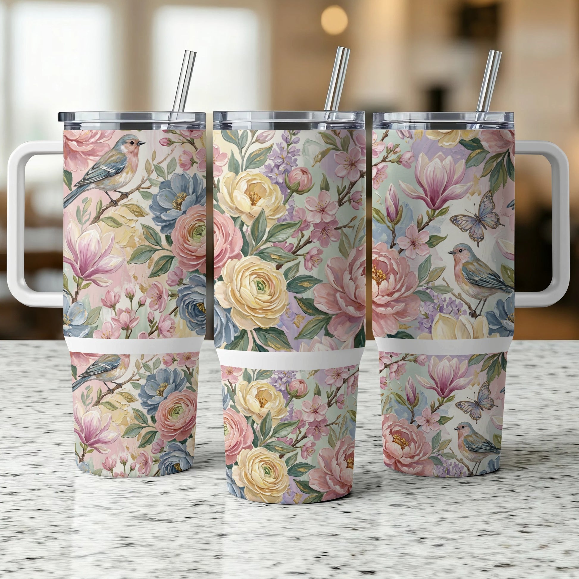 Three floral tumblers with birds and butterflies on a speckled countertop.