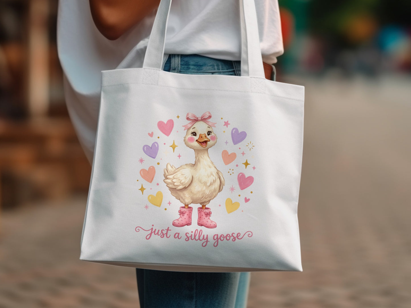 White tote bag with a cartoon goose wearing pink boots and hearts, saying "Just a silly goose."