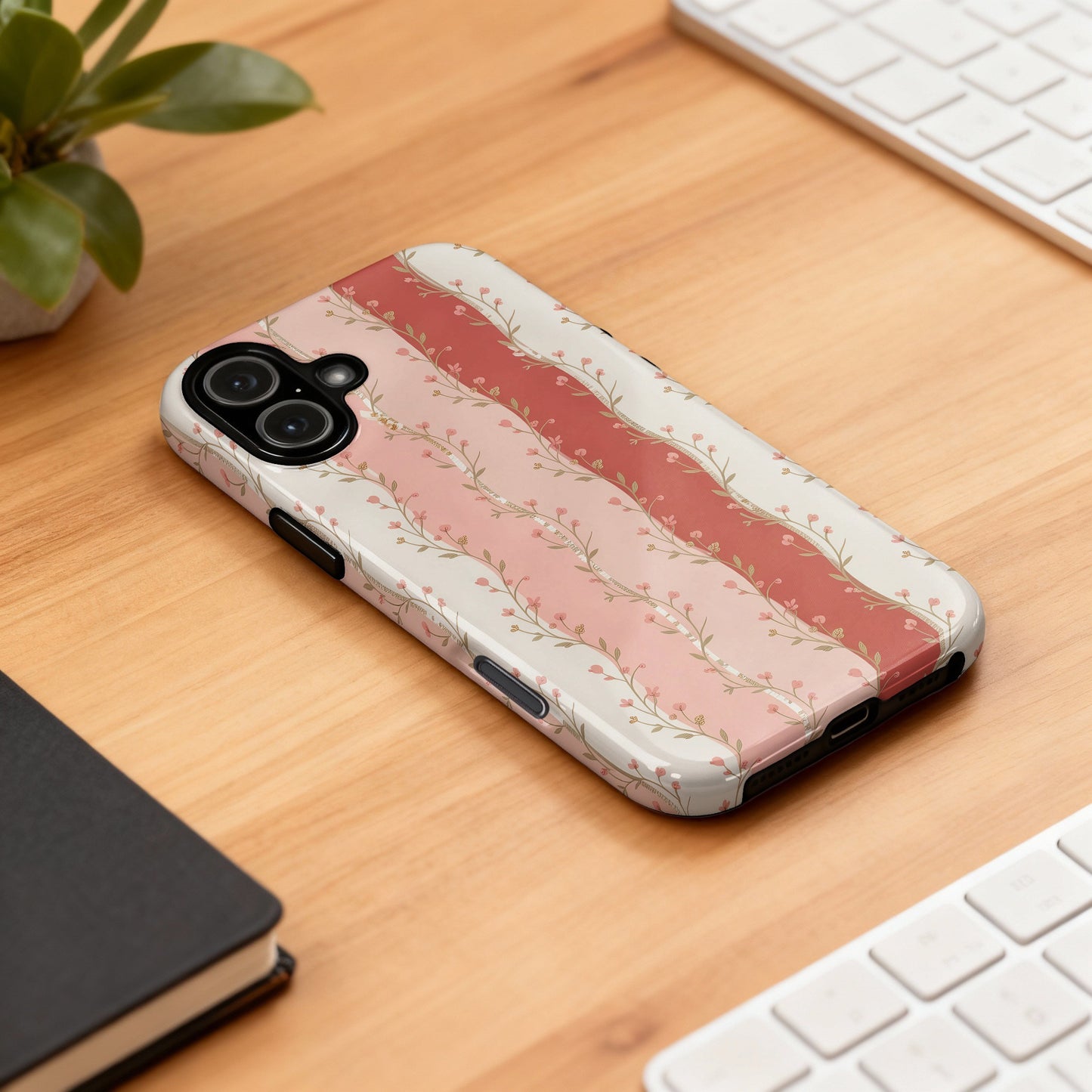 Phone case with pink floral stripes and scalloped edges on a wooden desk.