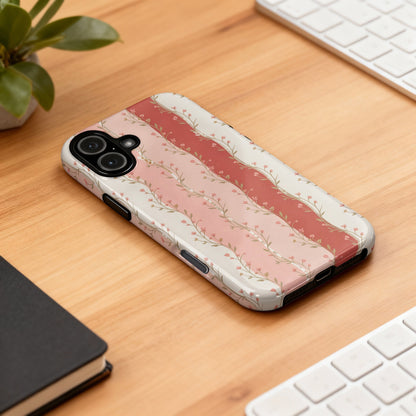 Phone case with pink floral stripes and scalloped edges on a wooden desk.