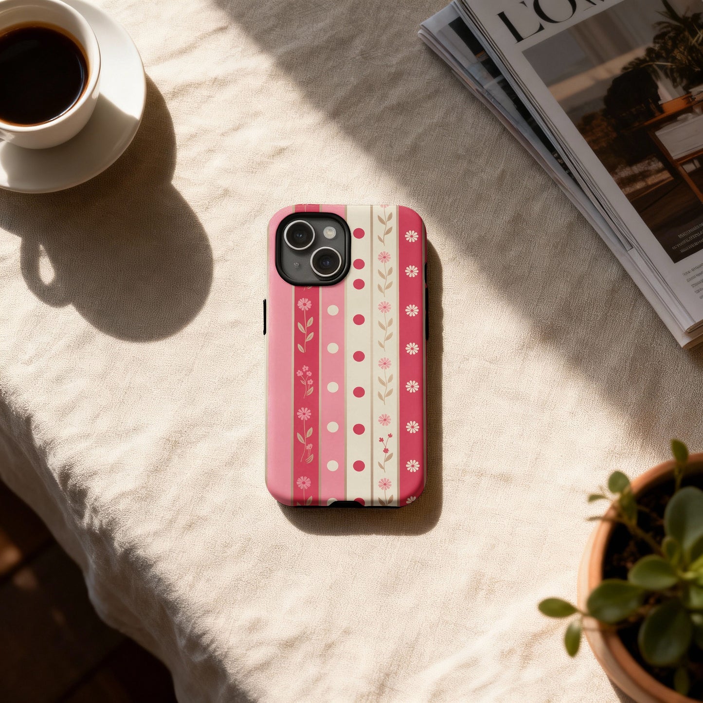 Pink and white floral striped iPhone case on a table with coffee and plant.