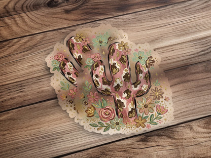 Cow print cactus sticker with floral accents on wood background.