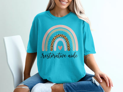 Teal t-shirt with rainbow design and text "restorative aide".
