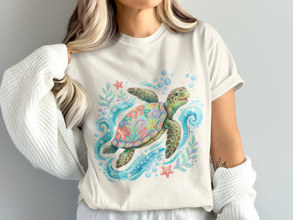 Watercolor sea turtle with flowers, bubbles, and starfish on a light cream t-shirt.