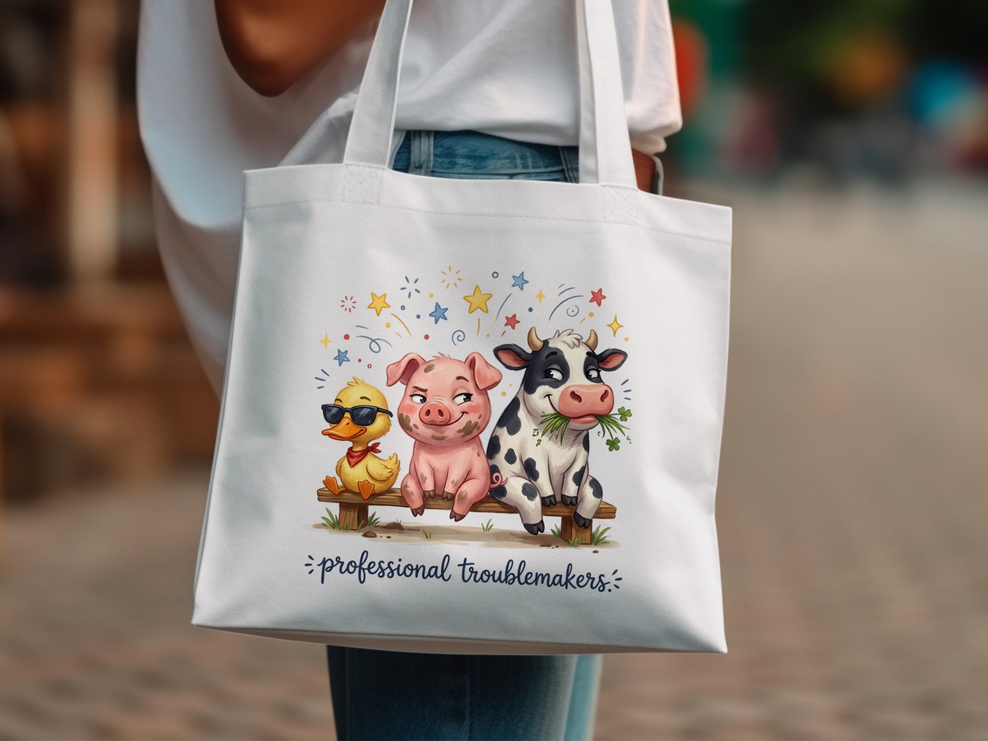 White tote bag with duck, pig, and cow illustration and text "professional troublemakers".