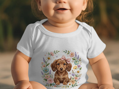 Baby wearing a white onesie with a watercolor illustration of a dachshund puppy.