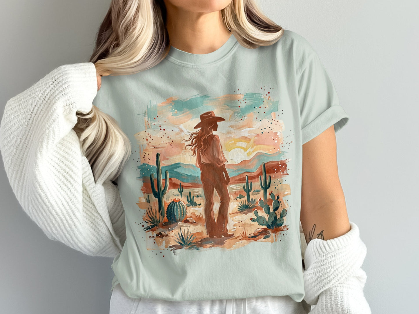 Woman wearing a light blue t-shirt with a desert landscape art print.