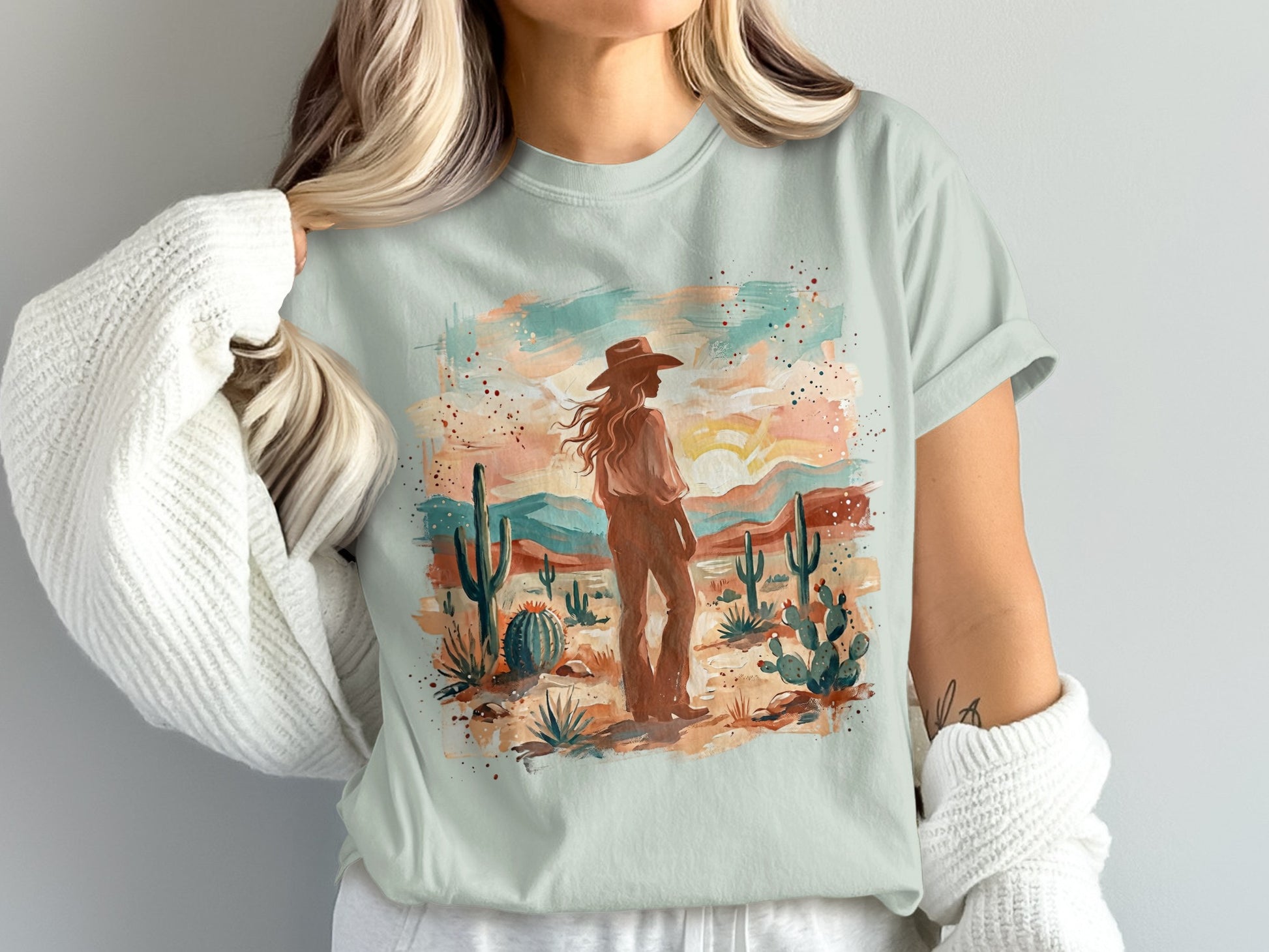Woman wearing a light blue t-shirt with a desert landscape art print.
